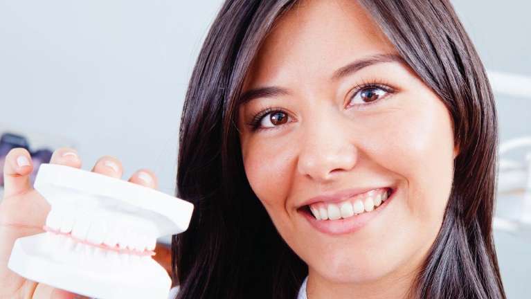 A smiling lady holding a model of a dental crown in Oatley, NSW.