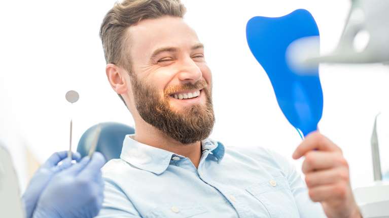 Man looking at himself in the mirror after after cosmetic dentistry session in Oatley, NSW